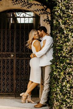 a man and woman embracing in front of an iron gate with ivy growing on it