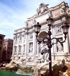 a street light next to a fountain in front of a building with statues on it