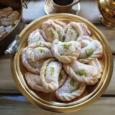 several pastries in a gold bowl on a wooden table next to cups and saucers