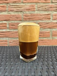 a glass filled with liquid sitting on top of a table next to a brick wall