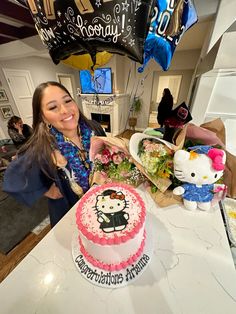 a woman standing in front of a cake with hello kitty on it and balloons above her