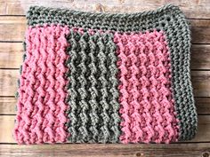 a crocheted dishcloth with pink and gray squares on it sitting on a wooden surface