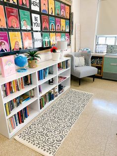 a room filled with lots of books on top of a white book shelf next to a gray chair