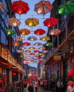 many umbrellas are hanging from the ceiling in an alleyway with people walking down it