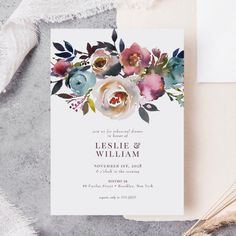 an elegant floral wedding card with watercolor flowers and greenery is displayed on a table