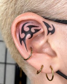 a person with tattoos on their ear and behind the ear is a pair of gold hoops