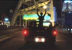 a man standing on the back of a truck in the middle of traffic at night