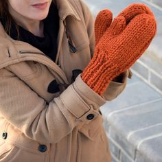 a woman wearing an orange knitted mitt on her left hand and looking at the camera