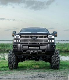 the front end of a black truck parked on top of a grass covered field next to a body of water