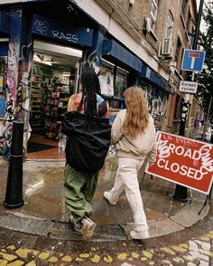 two women walking down the street in front of storefronts with graffiti on them