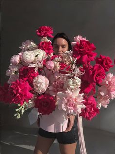 a woman holding a large bouquet of pink and white flowers in front of her face