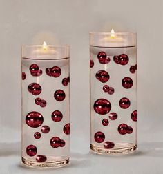 two candles with red balls in them sitting next to each other on a white surface