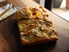 a piece of bread with lemons and herbs on it sitting on a wooden table