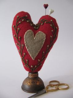 a pair of scissors and a red heart shaped object with gold trimmings sitting on top of a table