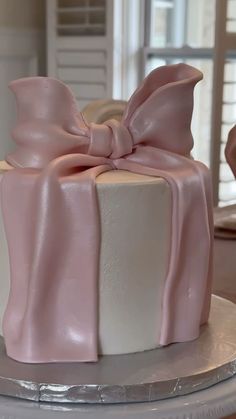 a pink and white cake with a large bow on it's top, sitting on a table