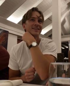 a man sitting at a table with a glass in front of him and his watch on his wrist