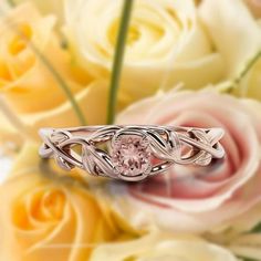 a pink diamond ring sitting on top of some white and yellow flowers with roses in the background