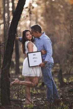 a man and woman standing next to each other in the woods holding a sign that says i will do