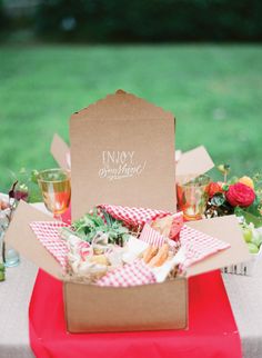 a table topped with a box filled with food next to a lush green park covered in trees