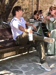 a man sitting on a bench next to a woman with a bottle in her hand