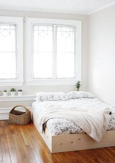 a simple bed frame in the corner of a room with hardwood floors and white walls