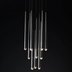 a chandelier made out of glass tubes hanging from it's ceiling in a dark room