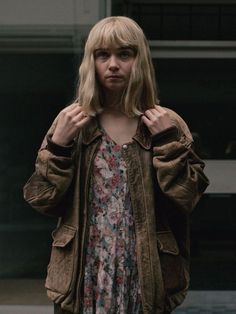 a woman standing in front of a building wearing a brown jacket and floral print dress