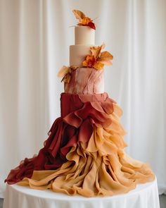 a three tiered wedding cake with red, orange and yellow ruffles on top