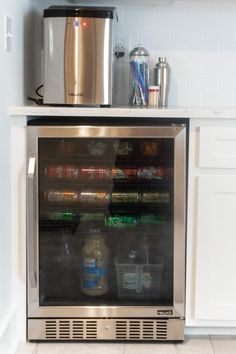 a stainless steel beverage cooler in the corner of a kitchen with white tile flooring