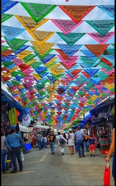 many colorful kites are hanging from the ceiling in an open air market with people walking under them