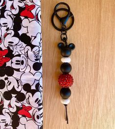 a mickey mouse keychain hanging on a wooden table with a red and white bead ball