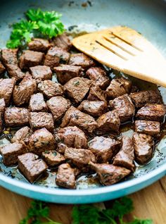 a bowl filled with meat and broccoli next to a wooden spoon on top of a table