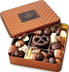 a box filled with assorted chocolates on top of a white table next to a cup