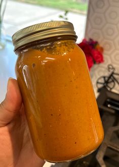 a hand holding a jar filled with orange colored liquid on top of a stovetop