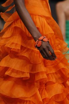 an orange dress with ruffles on the bottom and hand in front, holding onto a red bracelet