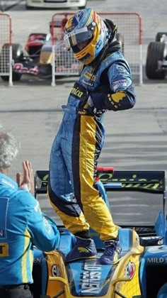 a man riding on the back of a racing car next to another person in blue and yellow