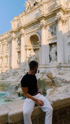 a man sitting on the edge of a wall next to a fountain in front of a building