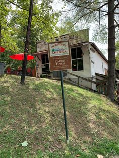 a sign in front of a small building on top of a grass covered hill next to trees