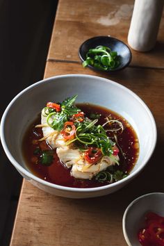 a white bowl filled with food on top of a wooden table next to two bowls