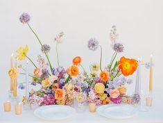 an arrangement of flowers and candles on a white table cloth with blue plates in the foreground