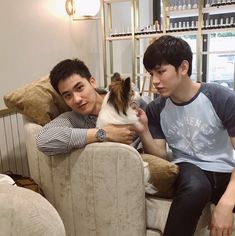 two young men sitting on couches with one holding a small dog in his lap