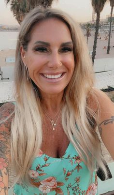 a woman with long blonde hair and tattoos on her chest smiling at the camera while standing in front of palm trees