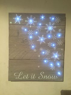 a wooden sign with snowflakes on it that says let it snow in white lights