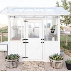 a small white shed with two planters on the front and one in the back