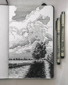 a notebook with a drawing of a tree and clouds in the sky next to two markers