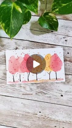 a card with watercolor trees on it next to a potted plant and scissors