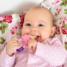 a baby is chewing on a toy while laying in a bed with pink and green floral sheets