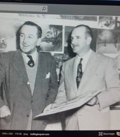 two men standing next to each other in front of a computer screen and holding papers