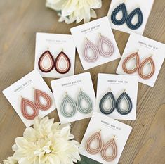 six pairs of earrings are displayed on a table next to some flowers and a card