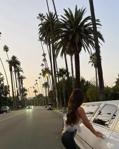 a woman leaning on the hood of a car in front of palm trees and parked cars